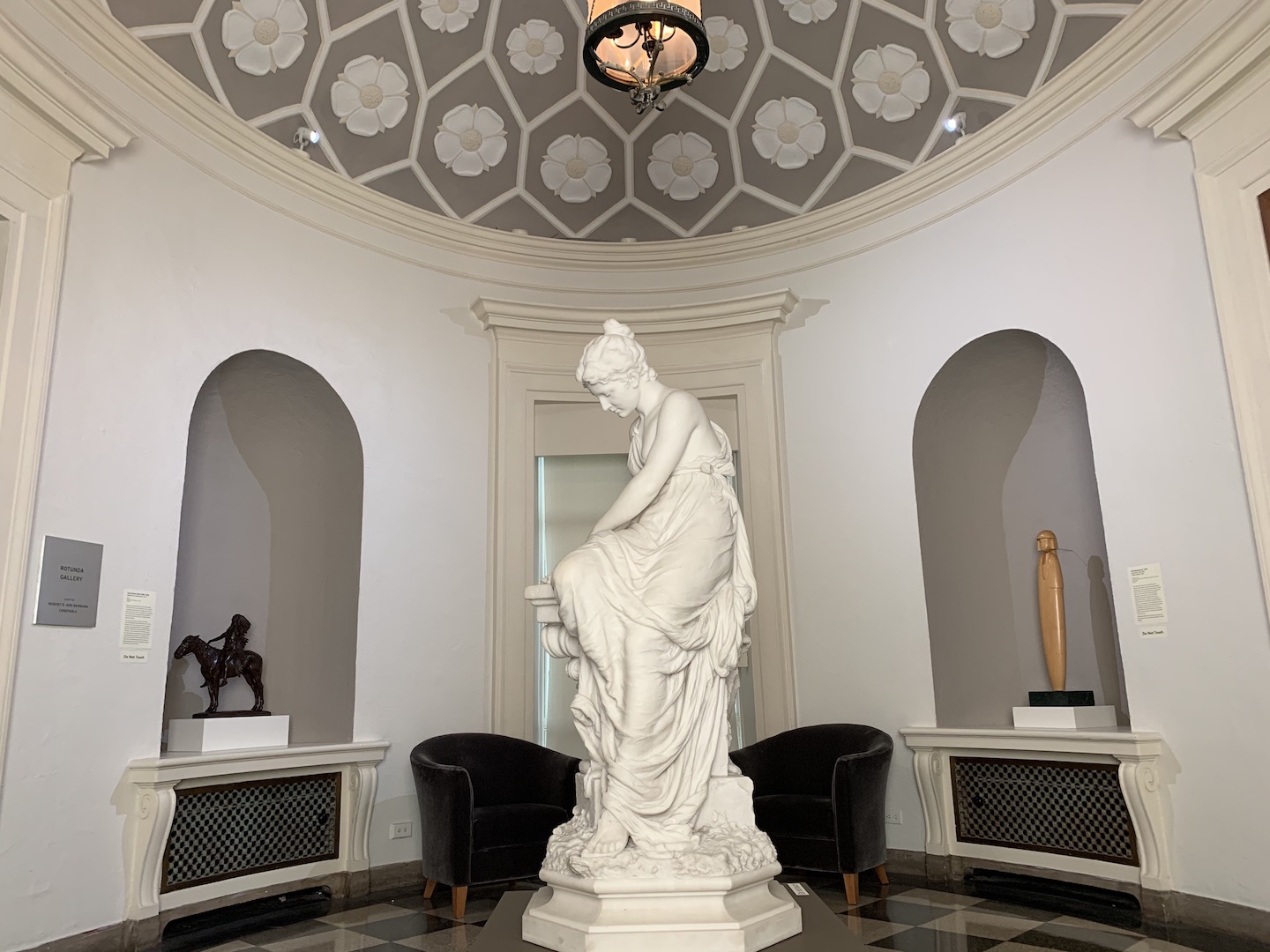The rotunda gallery at MM, a small round gallery. In the center is a marble sculture showing a woman creating a crown out of olive branches. 
