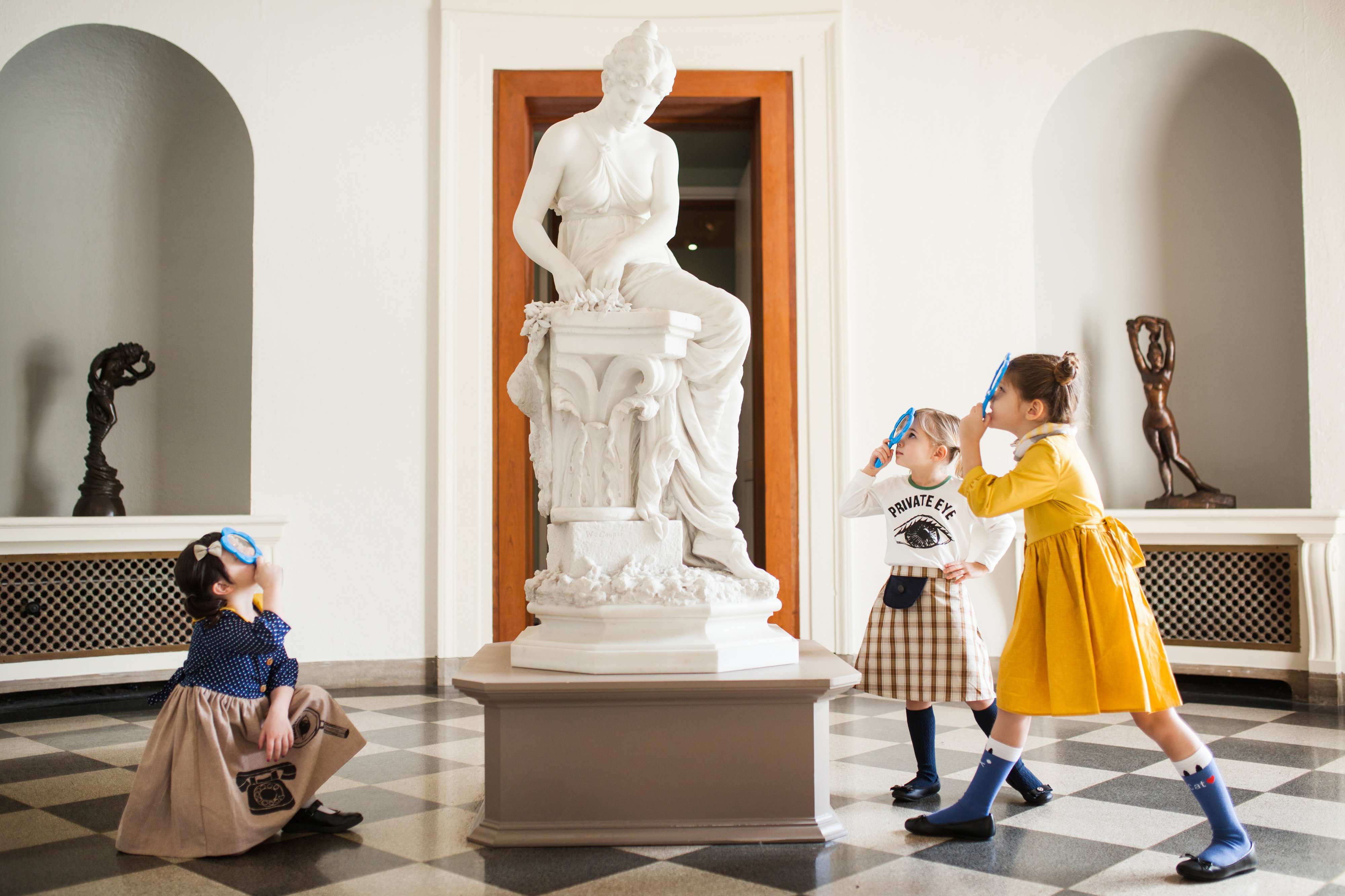Three girls with magnifying glasses examining the statue in MAM's Rotunda Gallery