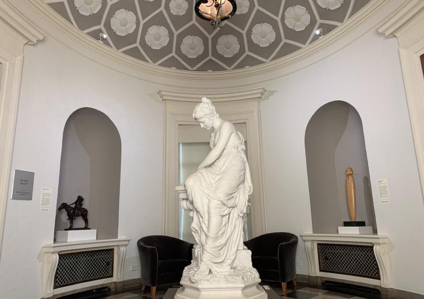 The rotunda gallery at MM, a small round gallery. In the center is a marble sculture showing a woman creating a crown out of olive branches. 