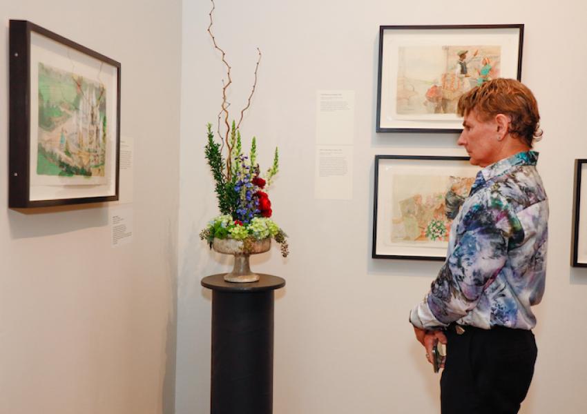 An Art in Bloom Luncheon attendee focusing on a floral arrangement in front of the artwork that inspired it.