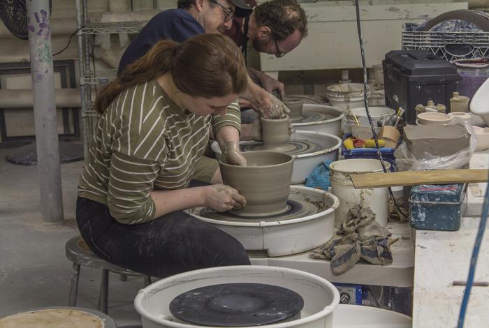 Advanced Wheel Throwing: View from the side as a student sits at their potter's wheel. They are in the middle of throwing a large bowel, one hand is inside the vase, while the other holds the vessel steady on the outside.
