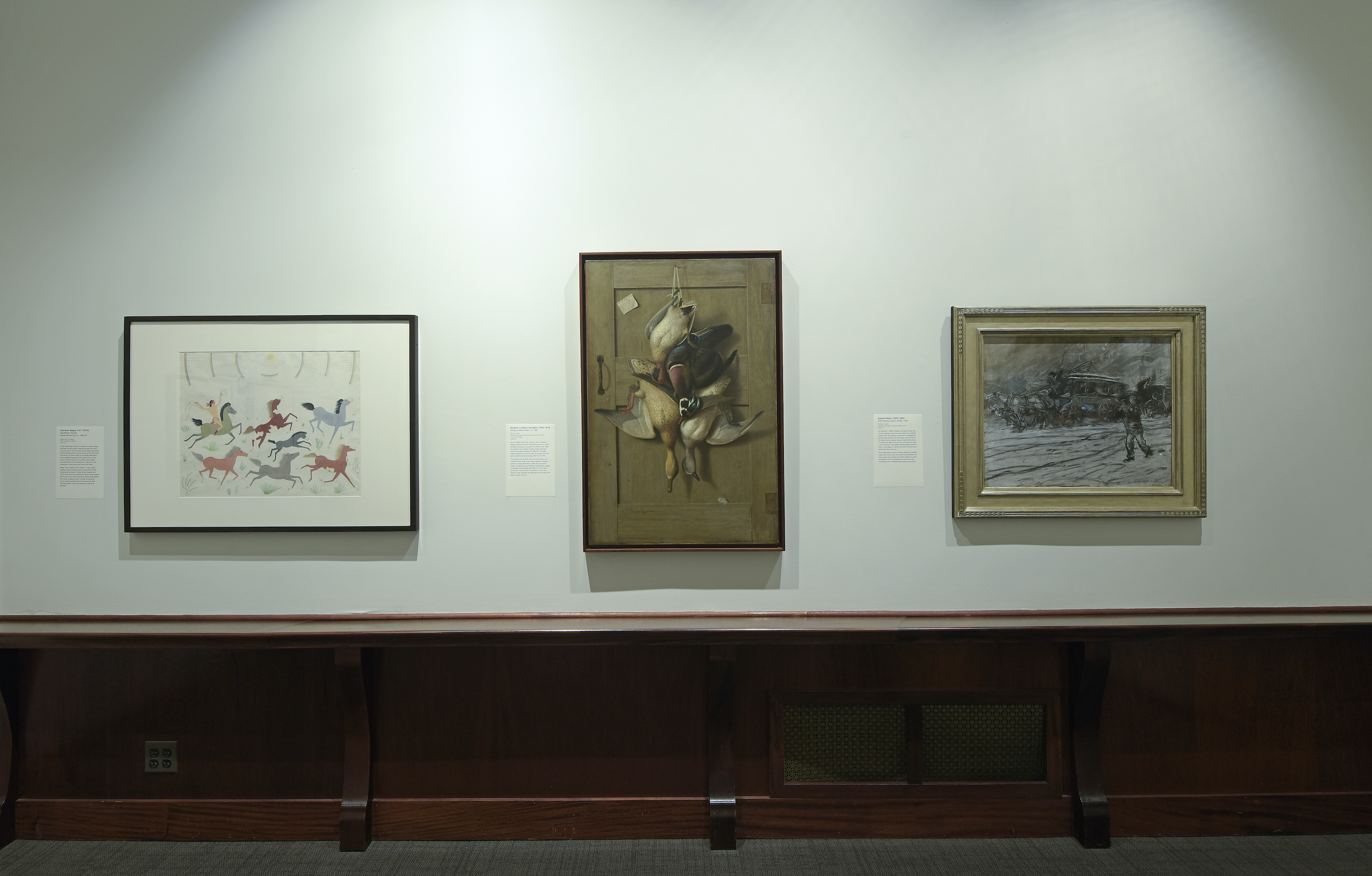 A wall in the uncaged gallery with three paintings hanging.