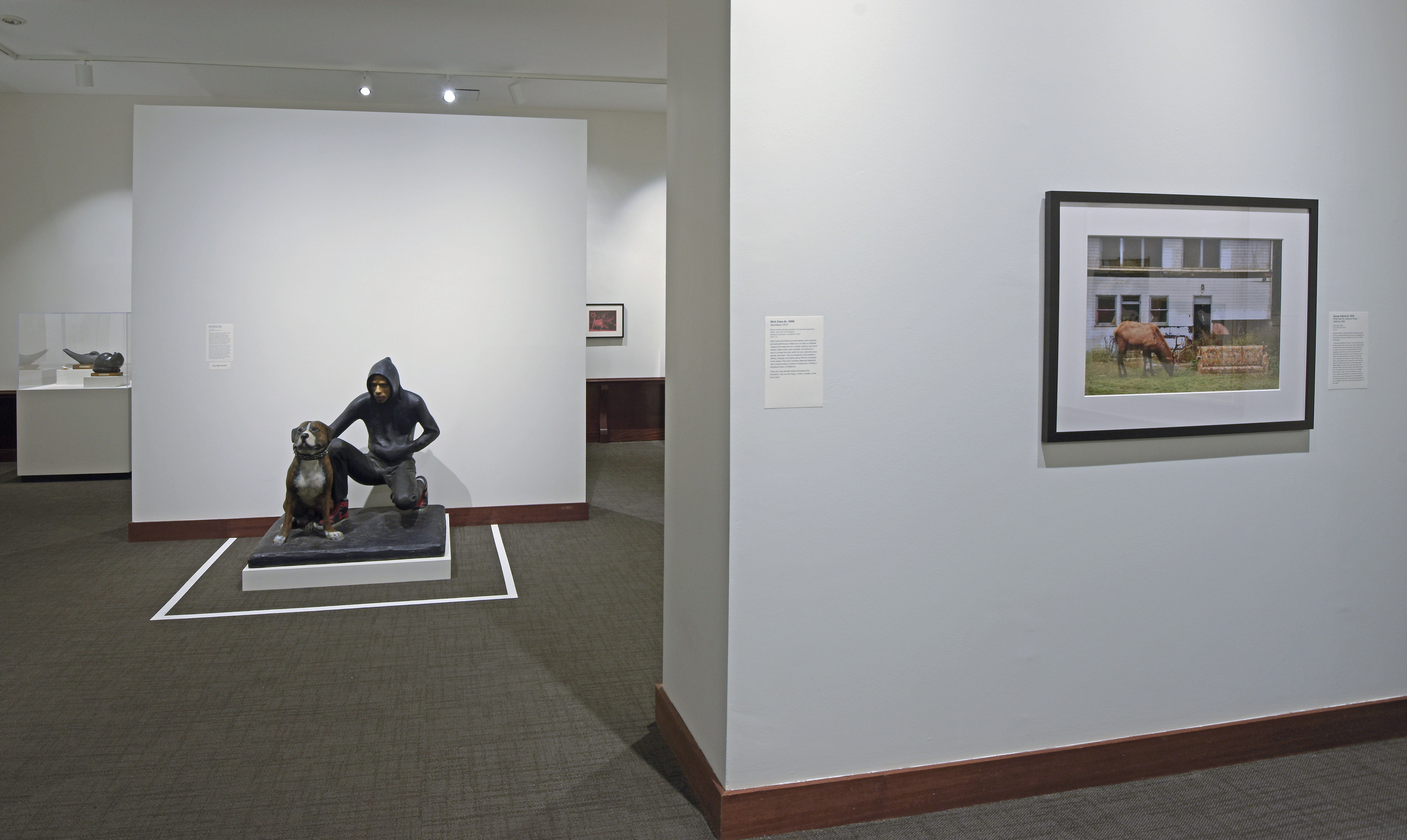 Gallery view in the uncaged exhibition. A painting and a sculpture of a teen and dog are in view.