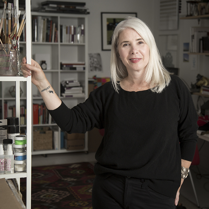 Maggie Meiners smiling at the camera, resting her hand on a shelf to her right.