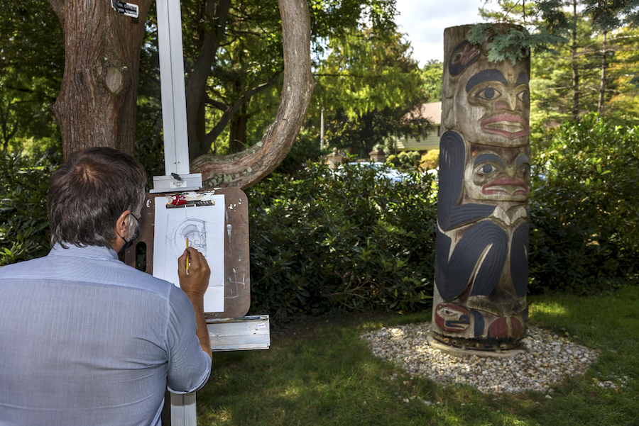 A visitor is sketching on an easel in front of one of MAM's outdoor sculptures.