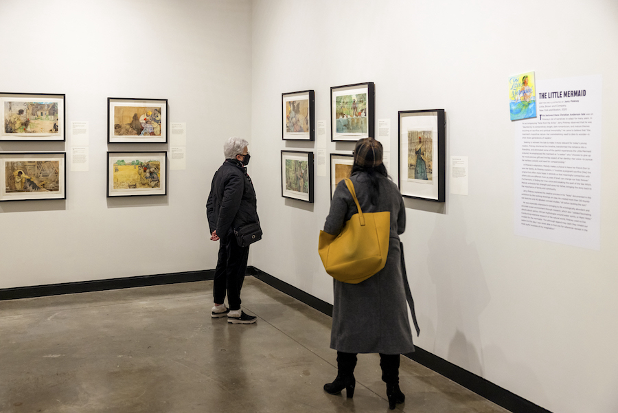 In MAM gallery, a visitor is looking at Pinkney's illustrations on a wall, and another visitor is walking toward the first.