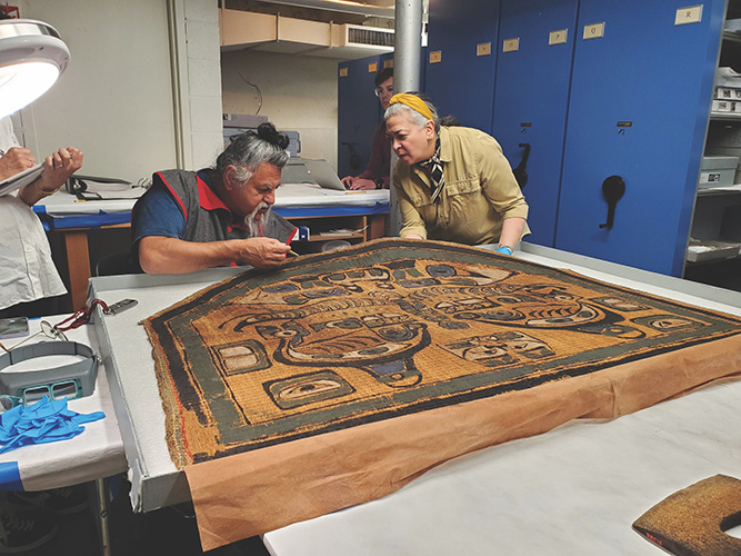 Artist, Scholar, and elder Haa’yuups (Nuu-chah-nulth) and Chief Registrar and Exhibition Designer Osanna Urbay review a 19th-century Nuu-chah-nulth cedar bark cape in MAM’s collection, June, 1, 2023
