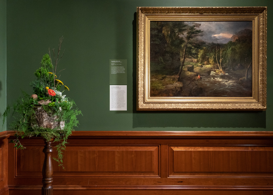 A floral arrangement sits in front and to the left of an artwork in the MAM galleries. This is part of a biennial celebration of floral design.