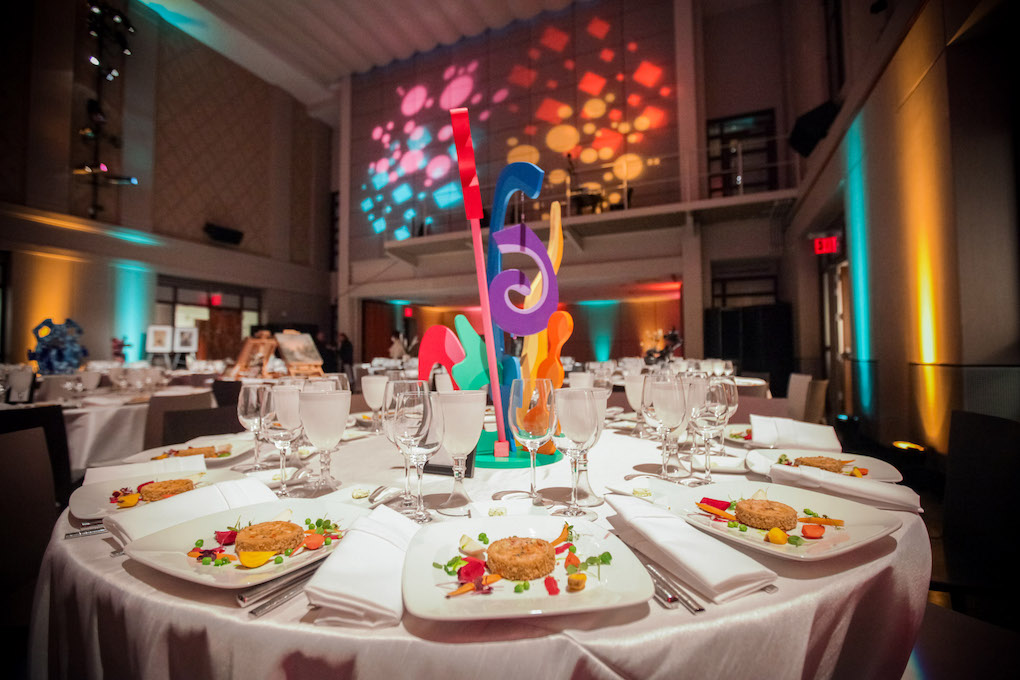 A beautifully set dinner table with artistic centerpiece, elegant glassware, and vibrant lighting in a stylish event space.