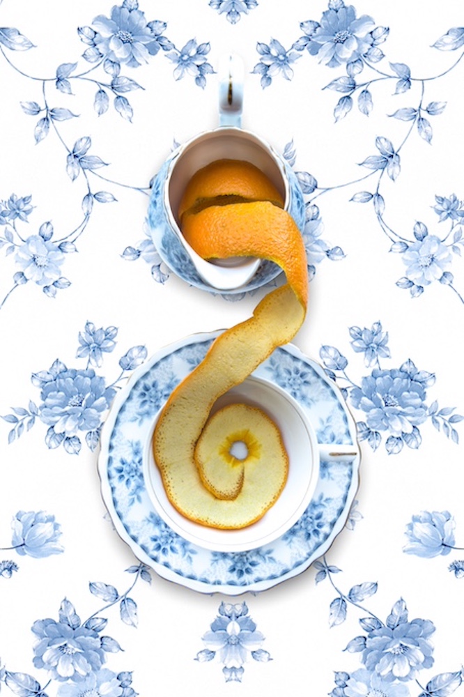 A curled orange peel elegantly spills from a teacup onto a decorative plate, set against a floral blue and white background.