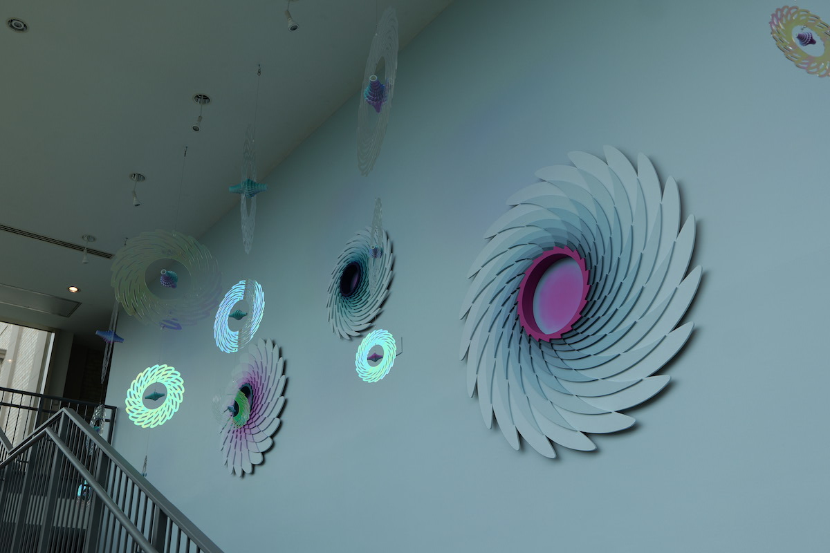 Colorful, swirling wall art made of layered shapes in shades of blue, pink, and white, creating a dynamic, modern visual effect.