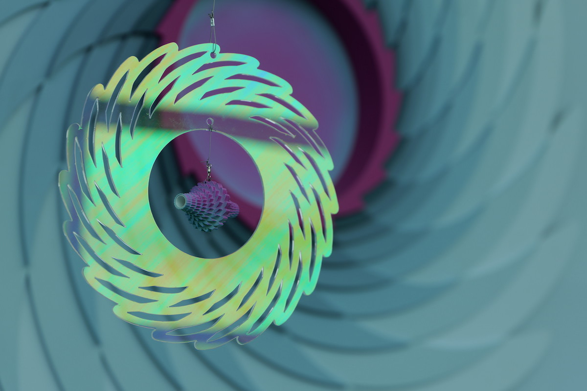 A colorful, swirling ornament features a wavy design, with a small, textured pendant hanging inside a larger circular frame.
