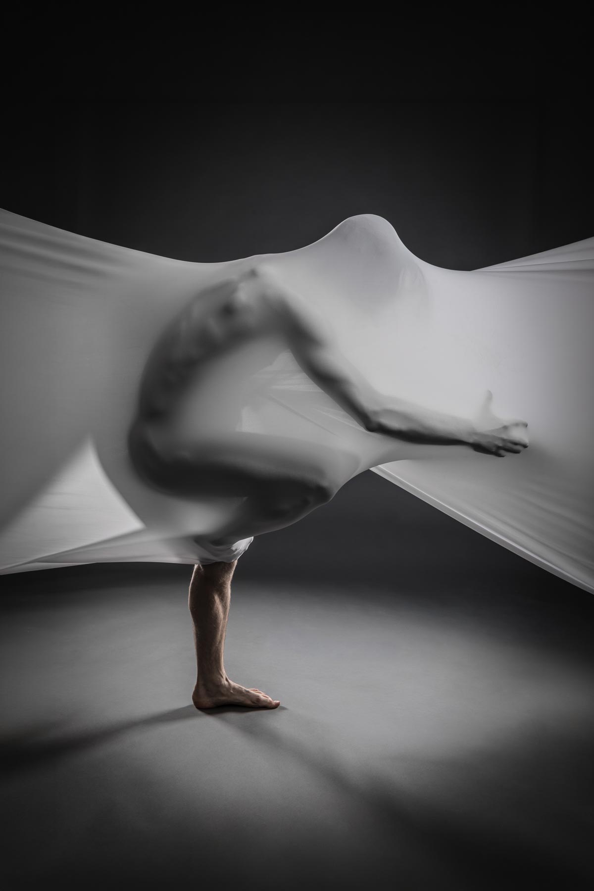 Black-and-white photograph of a figure moving beneath flowing fabric, the Pride Raffle prize