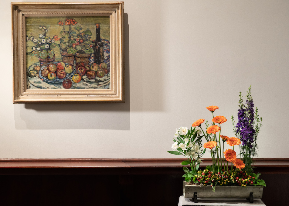 A floral arrangement sitting in front and to the left of an artwork in MAM's galleries. 