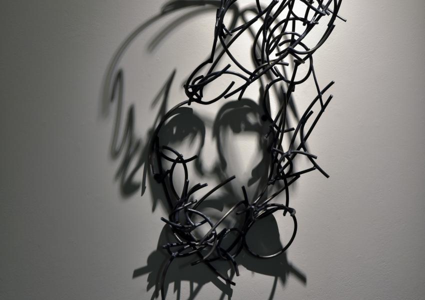Larry Kagan's metal sculpture hanging on the wall, casting a shadow that looks like a portrait of andy warhol.