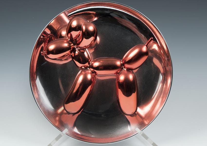 Small work by jeff koons made of metal that looks like a red balloon dog. 