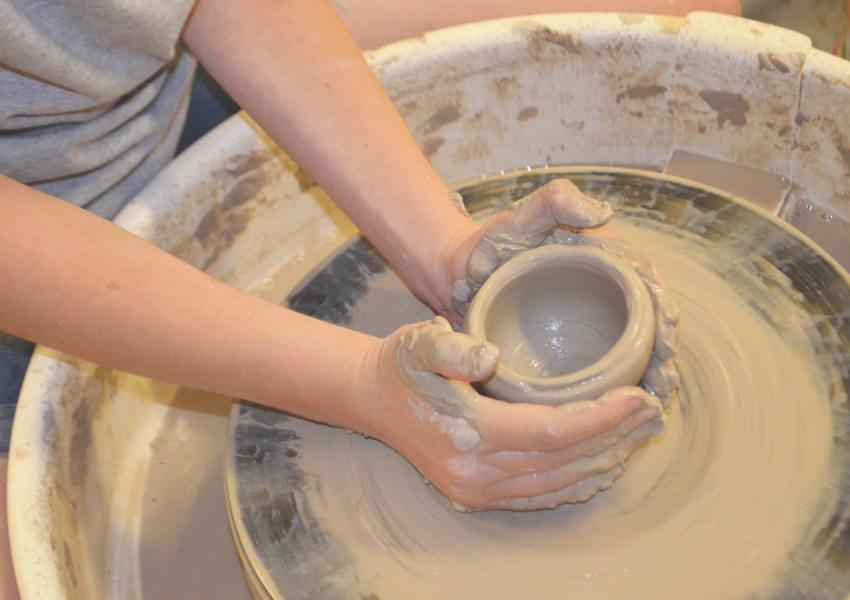 A student's hands working on the pottery wheel.