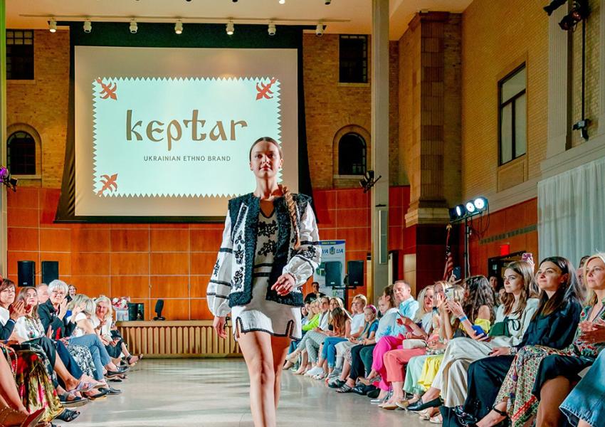 A fashion show with a model in traditional Ukrainian attire walking down the runway before an audience.