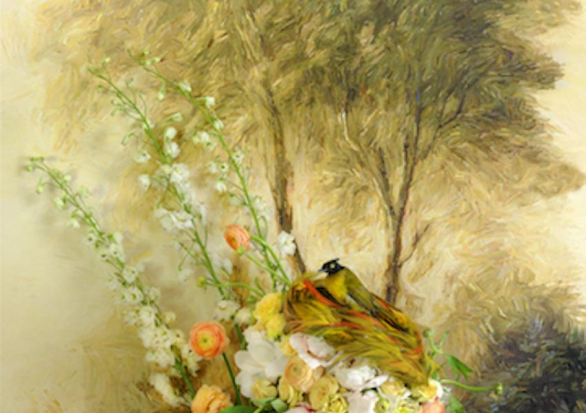 A vibrant floral arrangement with a yellow bird, set against a soft, painted landscape backdrop featuring trees and greenery.