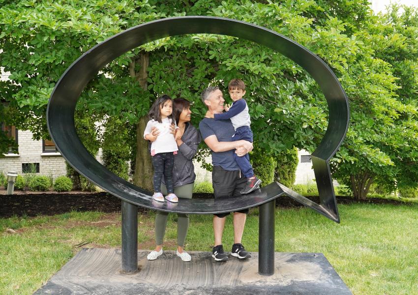 Family of four (two adults and two young children) standing in MAM's outdoor Speech Bubble Sculpture