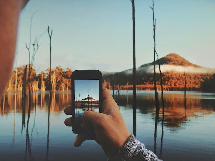 A person is taking a photo of an outdoor scene with a lake and a mountain on their iphone.