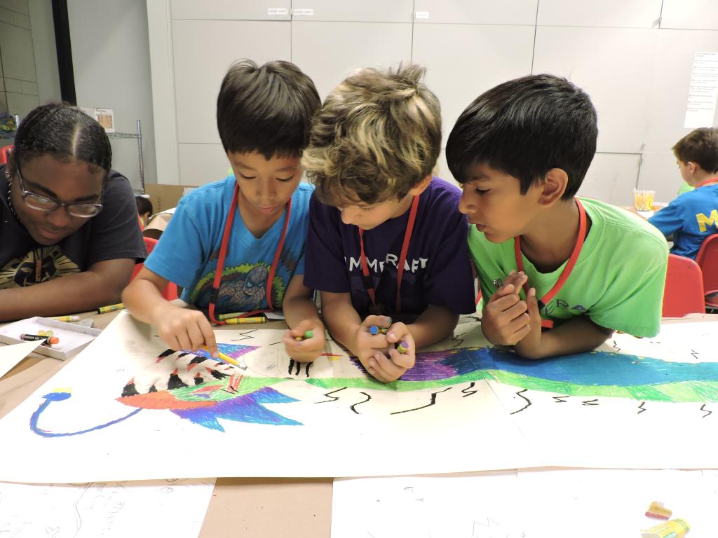 Three campers are working together on a drawing on a table.