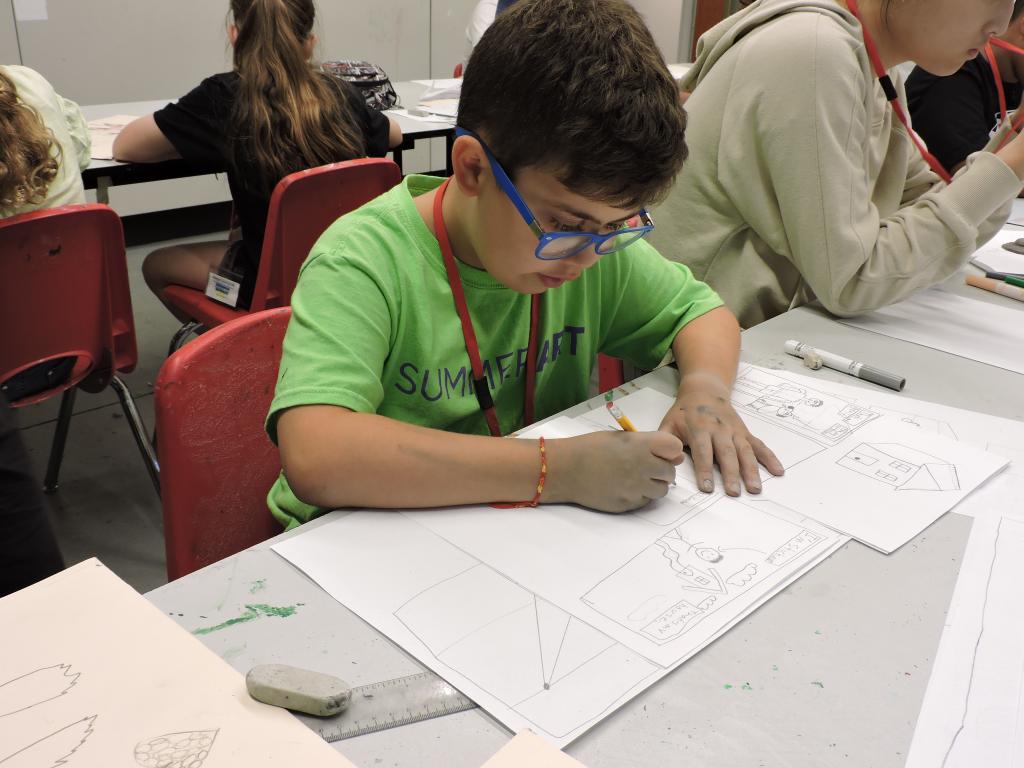 a student it drawing a comic strip on a large piece of paper. He is focused and looking at his work, not the camera.