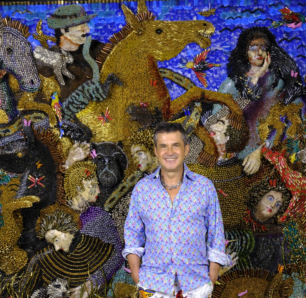 I'm an image! Federico Uribe standing in front of one of his works that features bullet shells turned into a vivid scene.