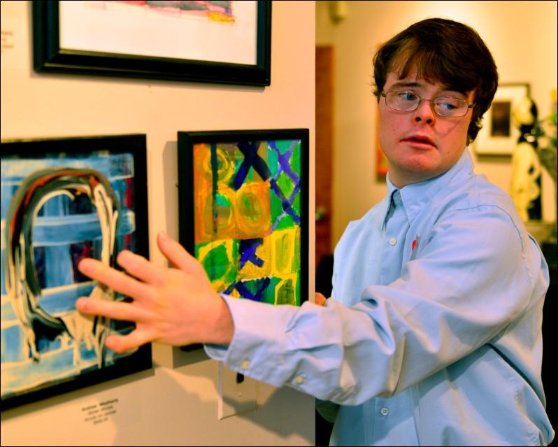 An artist is pointing to an artwork in the gallery on the left and looking to the right.