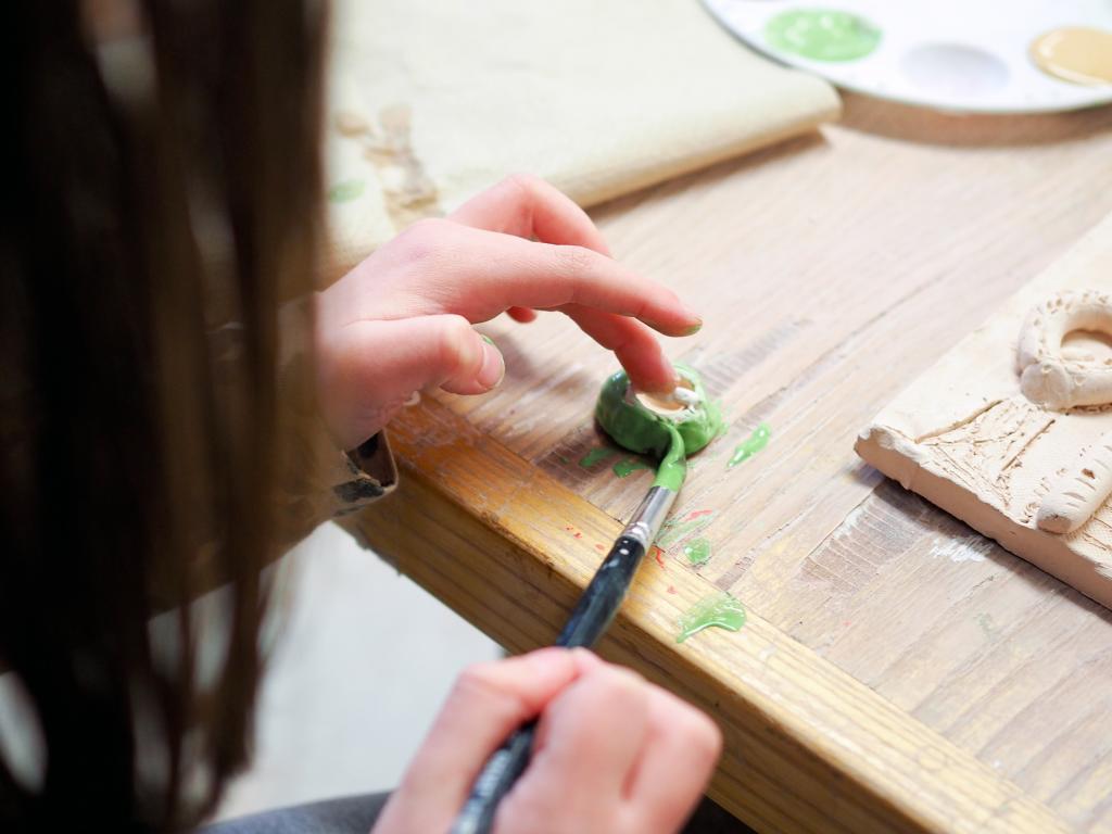 A child's hand painting glaze onto a clay piece
