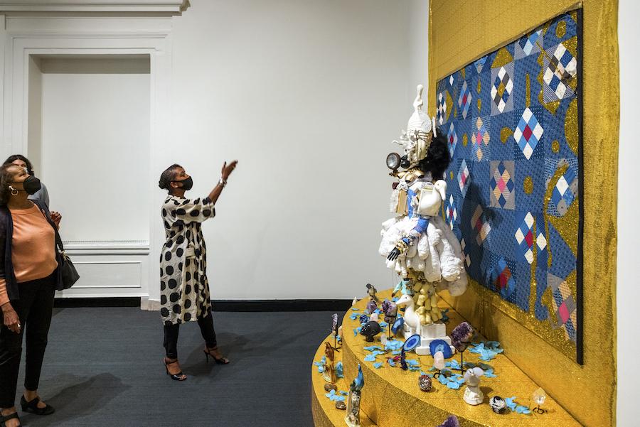 A visitor is gesturing toward a large installation work by Vanessa German in MAM gallery.