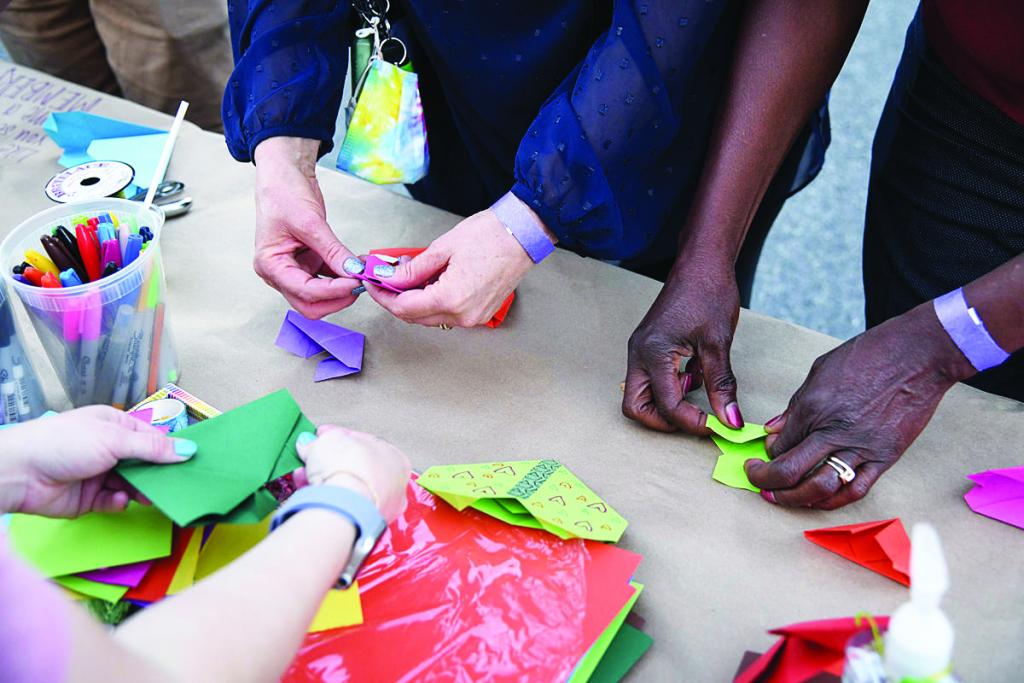 Many people's hands folding rainbow origami hearts. 