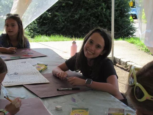 Camper smiling at camera as they are drawing as part of SummerART Drawing and Painting: In the Great Outdoors