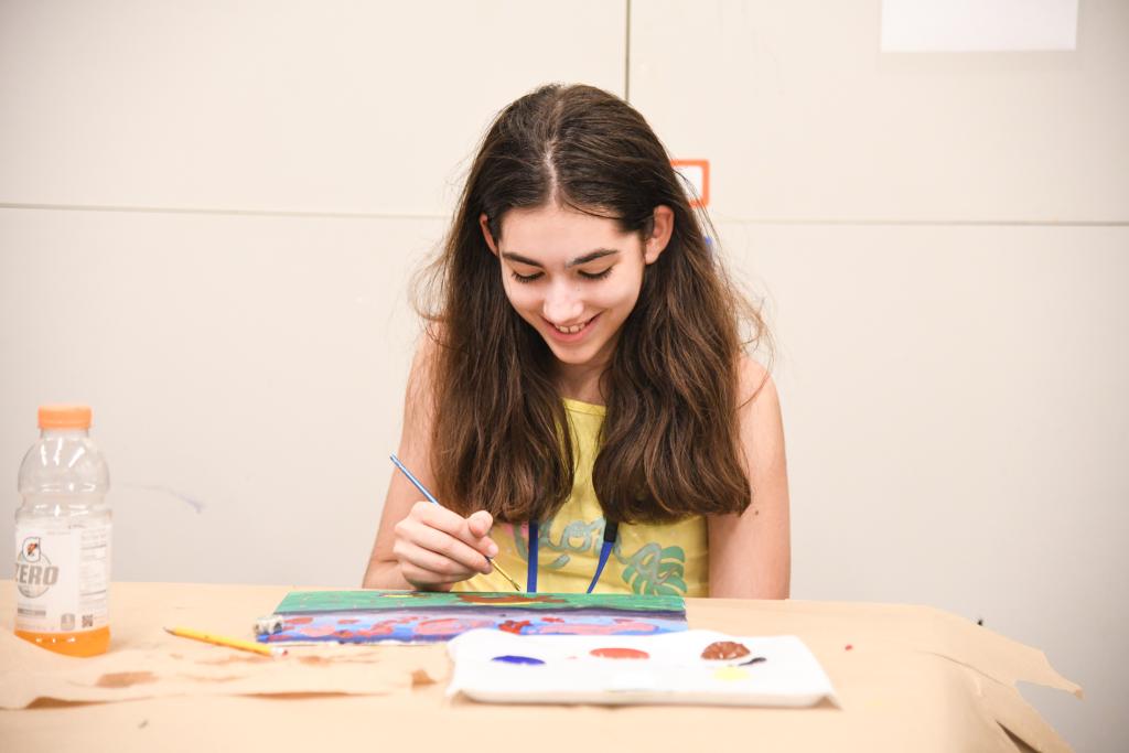 Front facing view of a student sitting at a table painting.