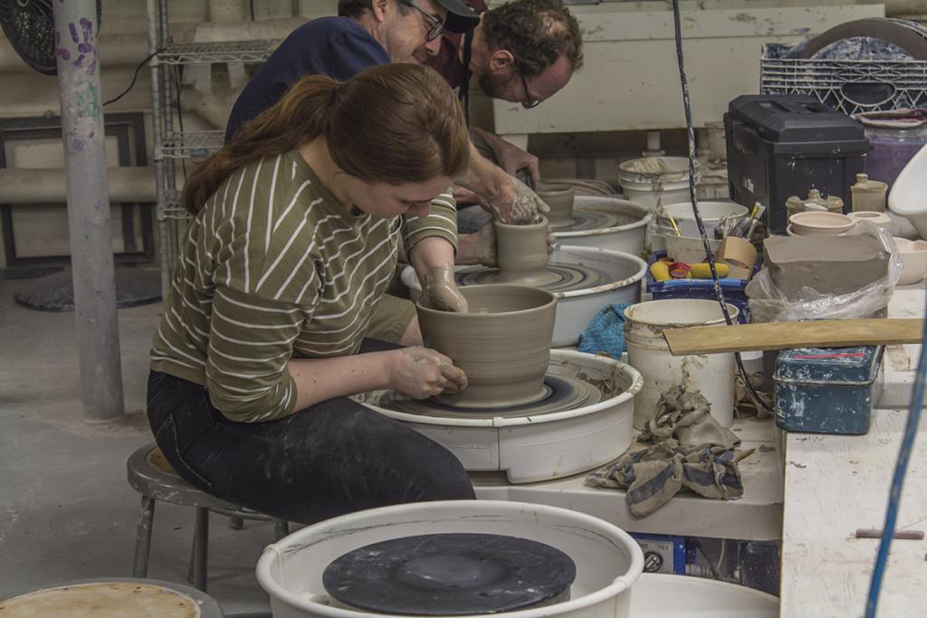 Advanced Wheel Throwing: View from the side as a student sits at their potter's wheel. They are in the middle of throwing a large bowel, one hand is inside the vase, while the other holds the vessel steady on the outside.