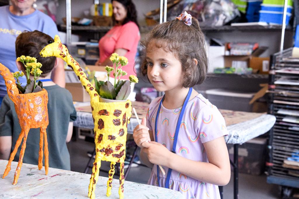 Child in a craft room with colorful giraffe-shaped planters.