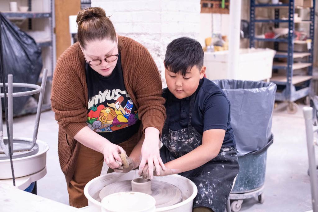 Two people working together on pottery wheel in a ceramic studio.