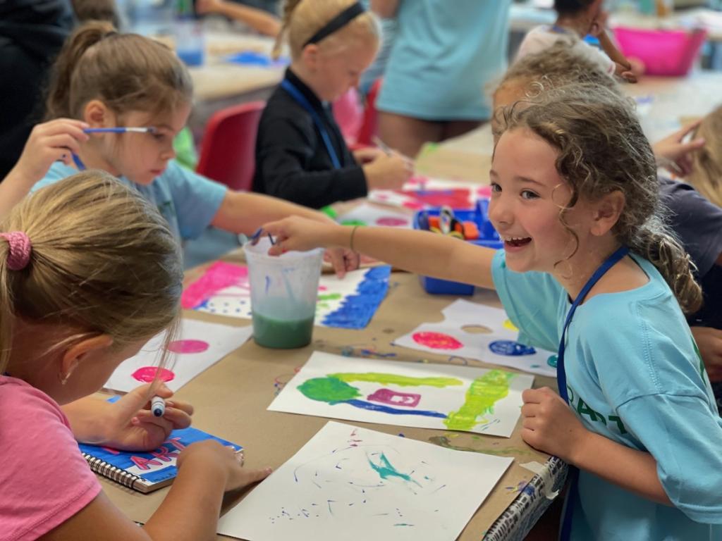 Children engaging in painting activities on tables with art supplies around.