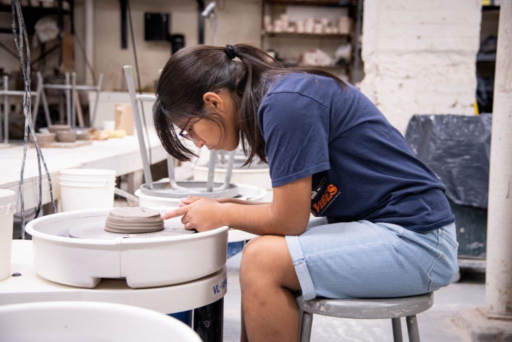 Person shaping clay on a pottery wheel in a workshop.