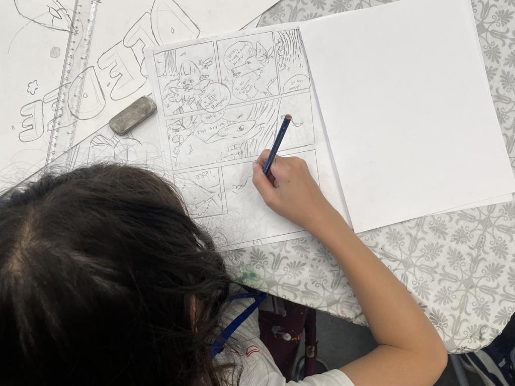 Person drawing a comic strip with a cat character on a paper.