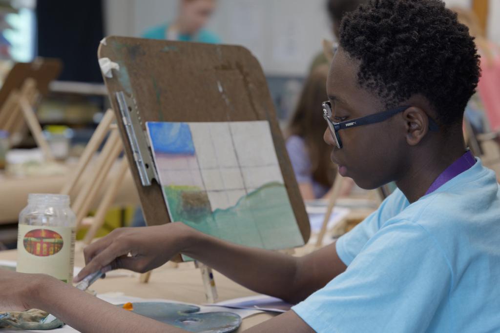 Person in a blue shirt painting on a canvas at an art class.
