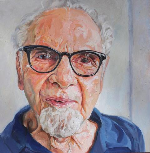 A portrait of an older man with white hair and a blue shirt, set against a softly colored background.