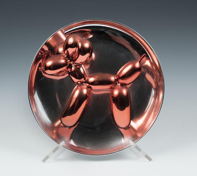 Small work by jeff koons made of metal that looks like a red balloon dog. 