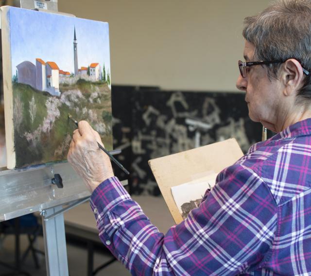 a woman is painting a landscape from a picture that she is holding for reference.