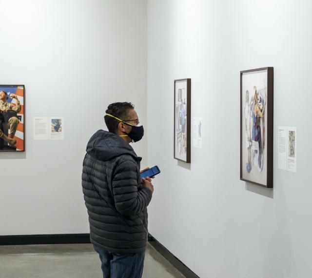 A visitor is looking at one of Meggie Meiners' works from the exhibition Fragile Freedoms: Maggie Meiners Revisits Rockwell.