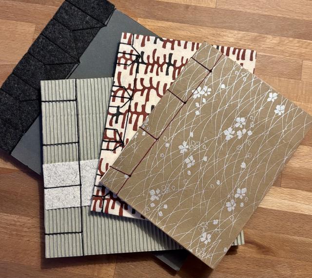 A stack of four handcrafted notebooks with diverse patterns and textures, resting on a wooden surface.