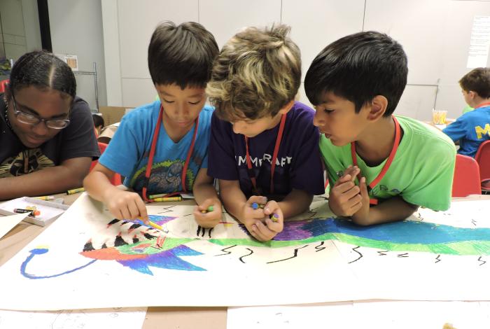 Three campers are working together on a drawing on a table.