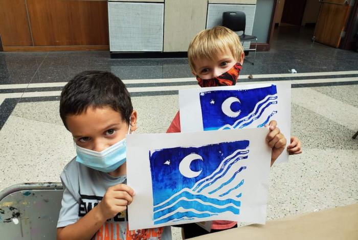 Two young students holding up their printed artwork for the camera.