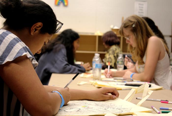 View of a group of teens sitting at a tale in a MAM studio, drawing