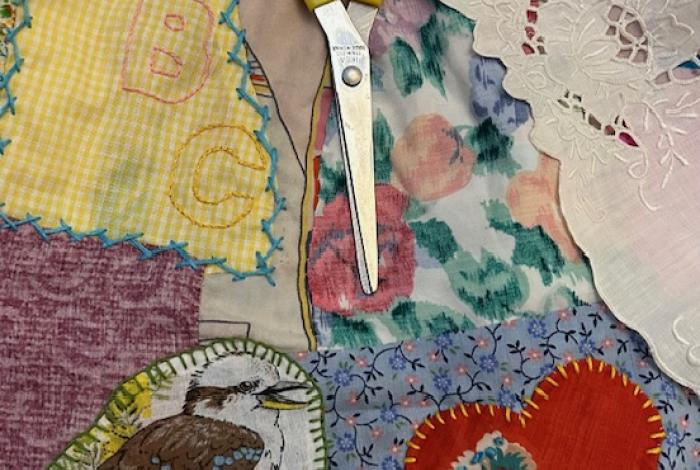 A pair of yellow scissors sitting on top of various pieces of fabric including motifs of a birds, heart, and letters, all of which are stitched into the fabric with visible stitches
